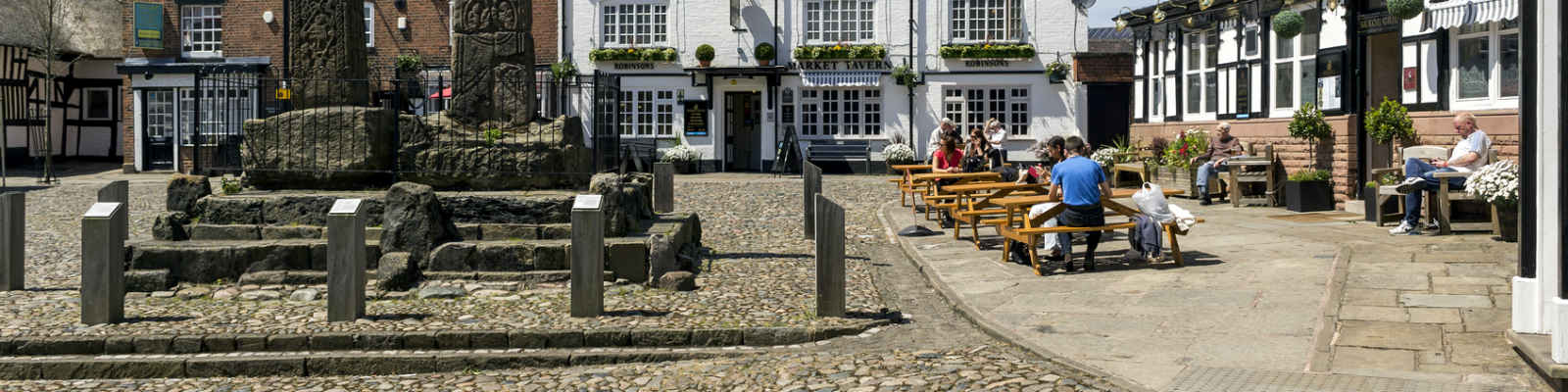 View of Sandbach town square, Cheshire. Two Anglo Saxon crosses can be seen and people can be seen sitting outside a public house.